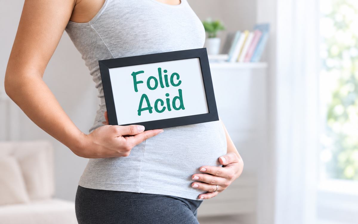 Pregnant woman holding a framed sign that reads Folic Acid